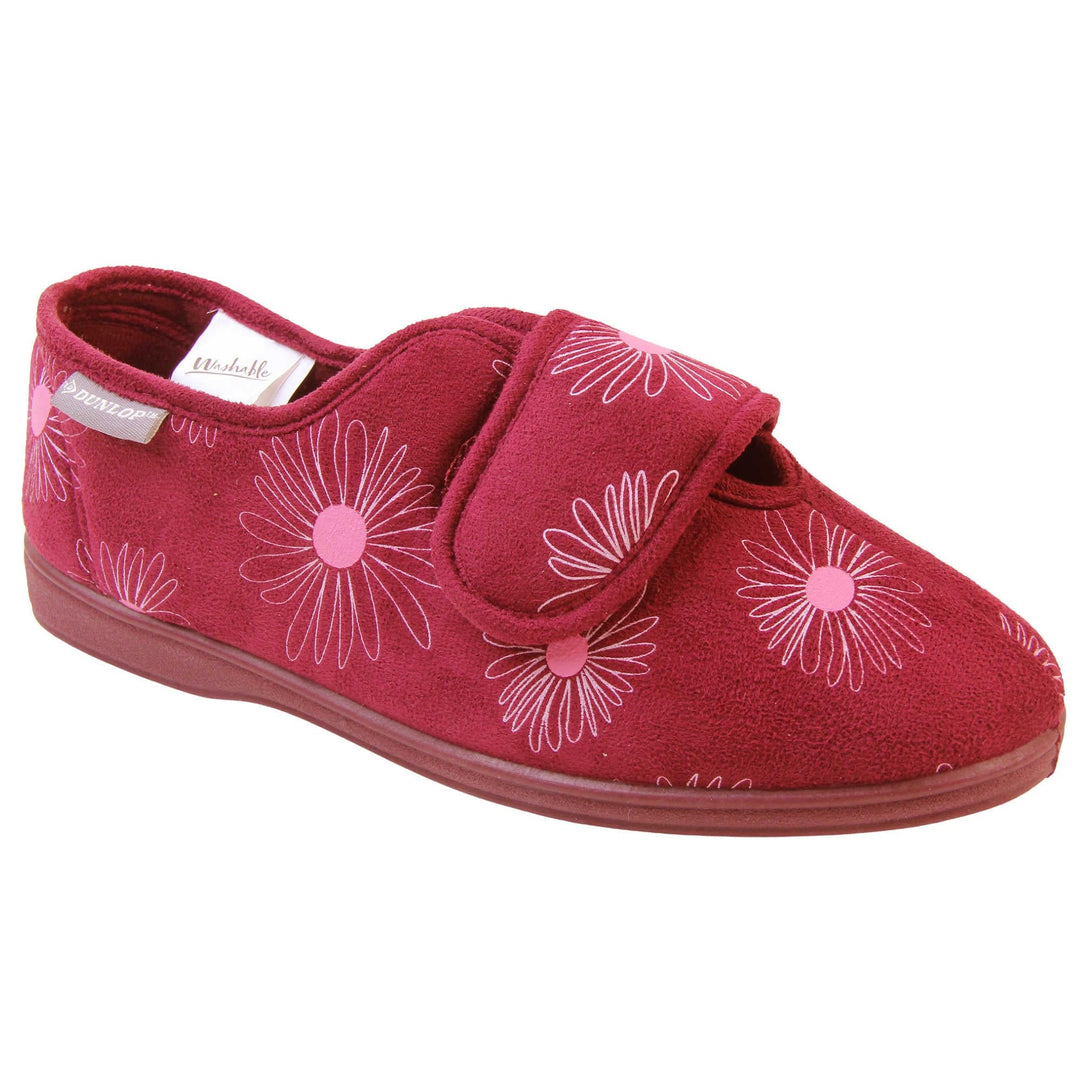 Slippers elderly women. Womens full back slipper. With a plum coloured upper with white daisy design and pink for the middle of the flowers. Touch fasten strap over the top of the foot to adjust the fit. Plum textile lining and firm plum sole. Right foot at an angle.