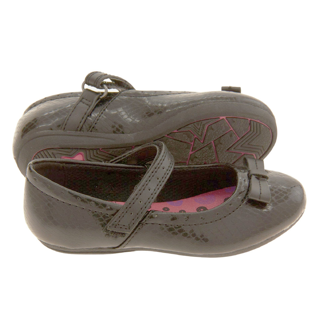 Girls Black School Shoes. Black Mary Jane shoes with a moc croc detail and a bow to the front. Black touch fasten strap over the foot and a pink insole. Both feet together from side profile but with the left foot on its side to show the sole.