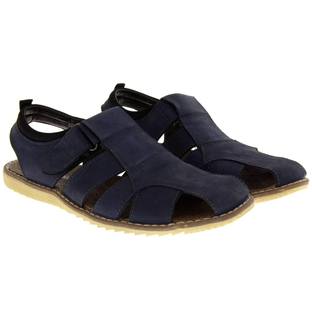Mens leather sandals. Classic sandal with a navy blue leather upper. Closed toe but with straps to give a cut outs down the side to keep feet cool. Touch close fastening ankle strap. With a brown insole and sand coloured outsole. Both feet together at a slight angle.