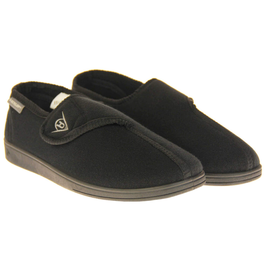 Adjustable comfort slippers. Full back slippers with black upper. Adjustable touch fasten strap to the top of the foot. Small grey label on the outside rim, with Dunlop branding in white. Black textile lining. Firm black sole. Both feet together at an angle.