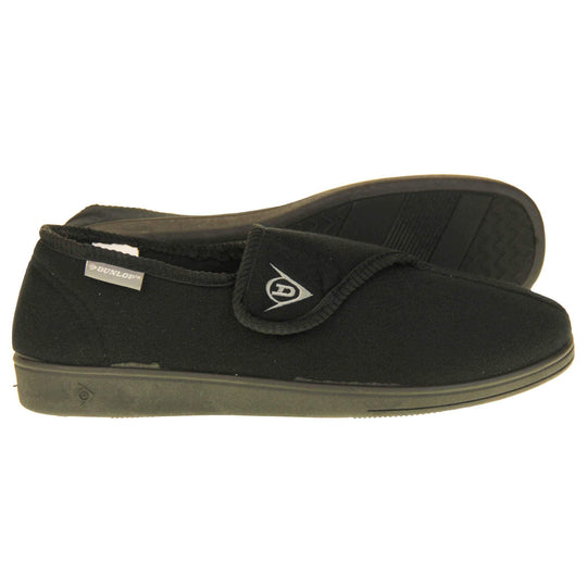 Adjustable comfort slippers. Full back slippers with black upper. Adjustable touch fasten strap to the top of the foot. Small grey label on the outside rim, with Dunlop branding in white. Black textile lining. Firm black sole. Both feet from side profile with left foot on its side to show the sole.