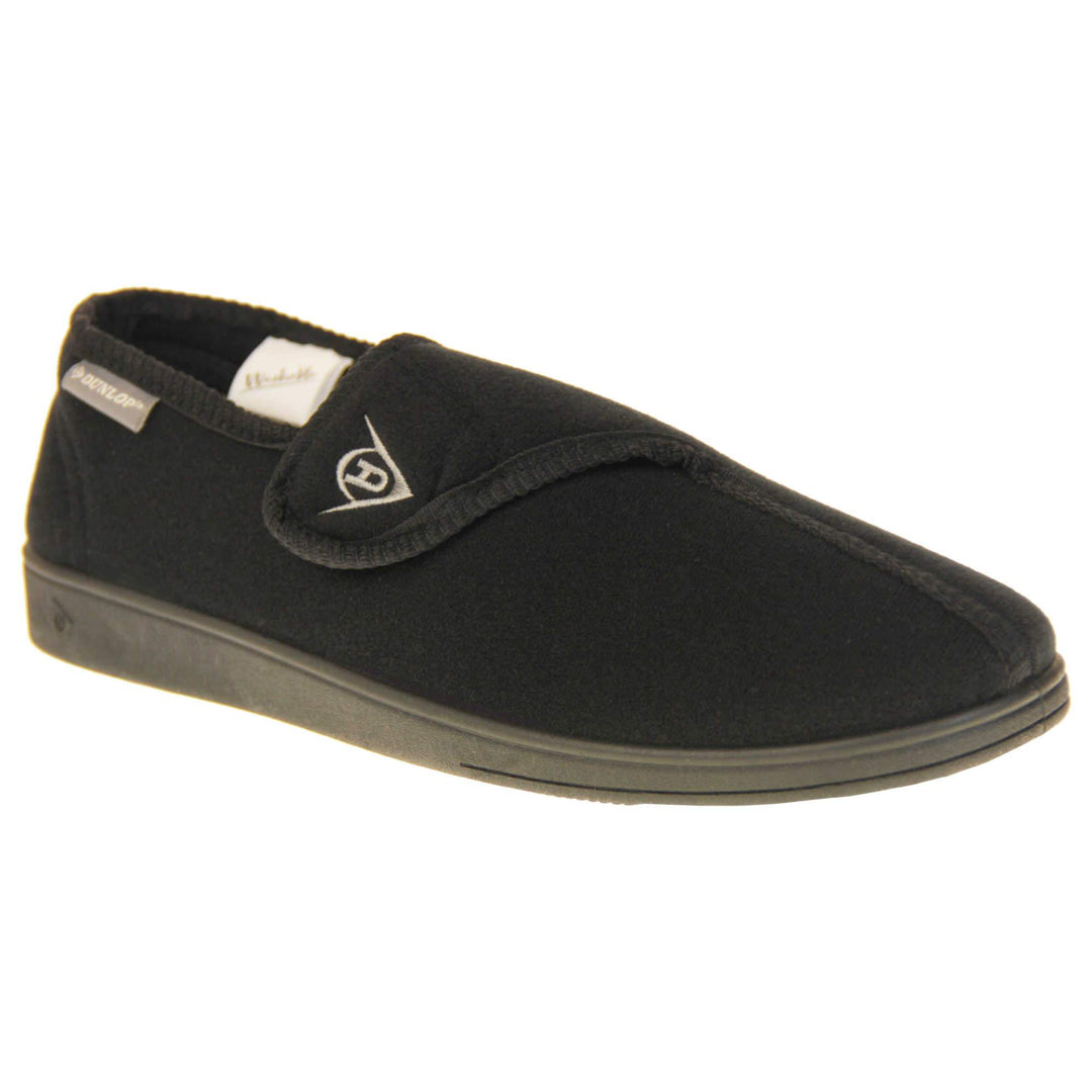 Adjustable comfort slippers. Full back slippers with black upper. Adjustable touch fasten strap to the top of the foot. Small grey label on the outside rim, with Dunlop branding in white. Black textile lining. Firm black sole. Right foot at an angle.