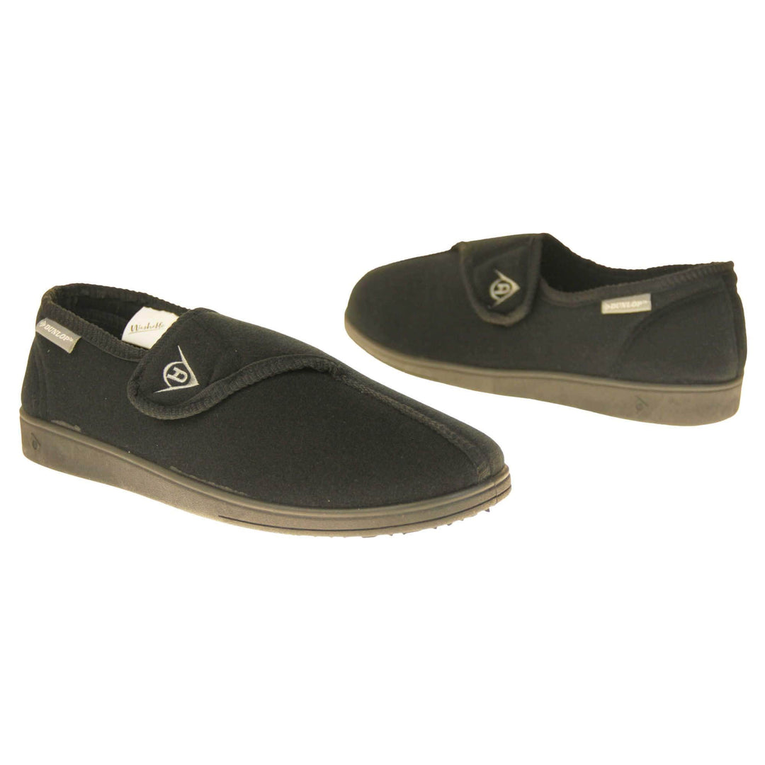 Adjustable comfort slippers. Full back slippers with black upper. Adjustable touch fasten strap to the top of the foot. Small grey label on the outside rim, with Dunlop branding in white. Black textile lining. Firm black sole. Both feet facing top to tail, at an angle.