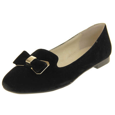 Ballerina loafer. Women's shoe in a ballerina style loafer with a black faux suede upper. Black bow with gold coloured metal backing and middle. Black sole with very small heel. Cream leather lining. Left foot at an angle.