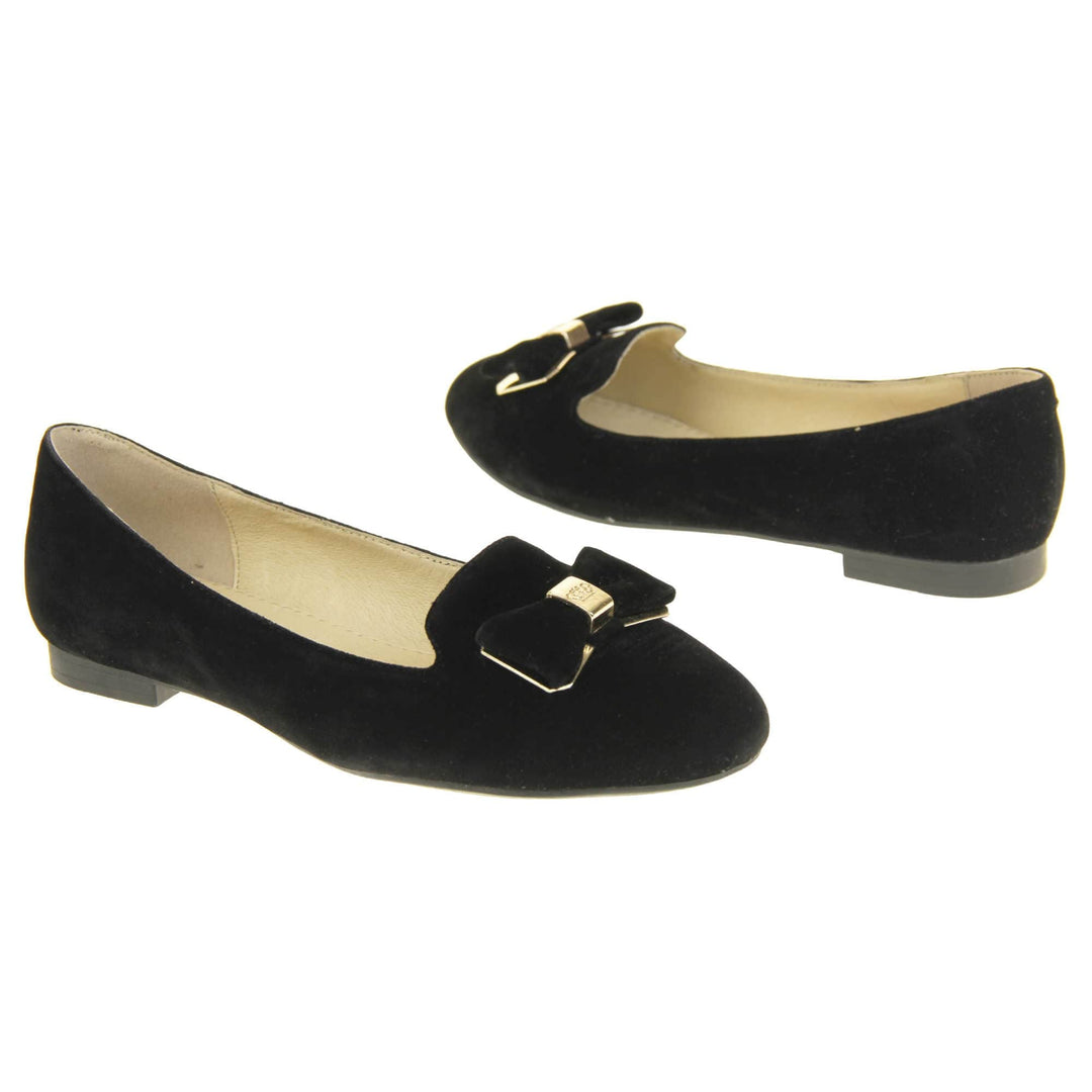 Ballerina loafer. Women's shoe in a ballerina style loafer with a black faux suede upper. Black bow with gold coloured metal backing and middle. Black sole with very small heel. Cream leather lining. Both feet at an angle facing top to tail.
