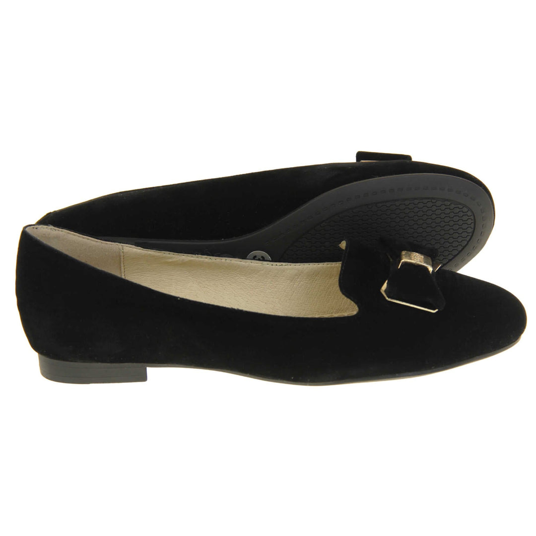 Ballerina loafer. Women's shoe in a ballerina style loafer with a black faux suede upper. Black bow with gold coloured metal backing and middle. Black sole with very small heel. Cream leather lining. Both feet from a side profile with the left foot on its side behind the the right foot to show the sole.