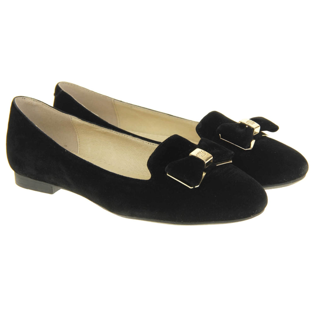 Ballerina loafer. Women's shoe in a ballerina style loafer with a black faux suede upper. Black bow with gold coloured metal backing and middle. Black sole with very small heel. Cream leather lining. Both feet together at a slight angle.
