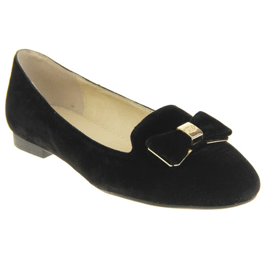 Ballerina loafer. Women's shoe in a ballerina style loafer with a black faux suede upper. Black bow with gold coloured metal backing and middle. Black sole with very small heel. Cream leather lining. Right foot at an angle.