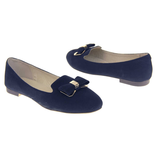 Ballet loafer. Women's shoe in a ballerina style loafer with a navy faux suede upper. Dark blue bow with gold coloured metal backing and middle. Brown sole with beige bottom with very small heel. Cream leather lining. Both feet at an angle facing top to tail.