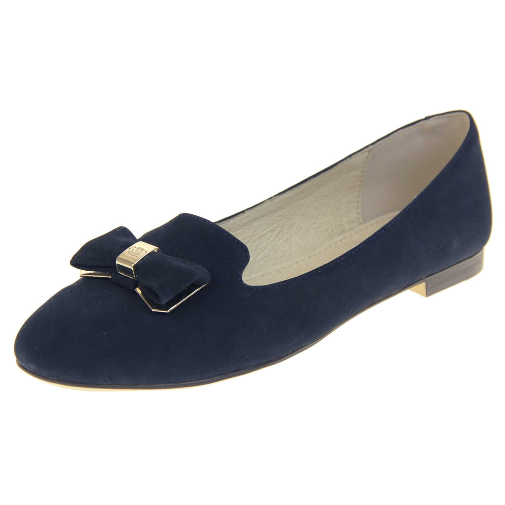 Ballet loafer. Women's shoe in a ballerina style loafer with a navy faux suede upper. Dark blue bow with gold coloured metal backing and middle. Brown sole with beige bottom with very small heel. Cream leather lining. Left foot at an angle.