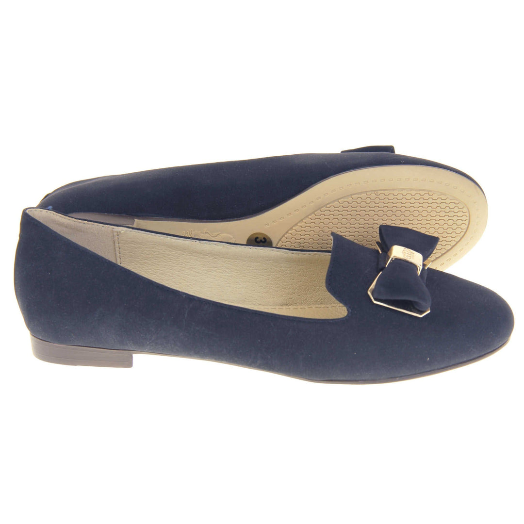 Ballet loafer. Women's shoe in a ballerina style loafer with a navy faux suede upper. Dark blue bow with gold coloured metal backing and middle. Brown sole with beige bottom with very small heel. Cream leather lining. Both feet from a side profile with the left foot on its side behind the the right foot to show the sole.