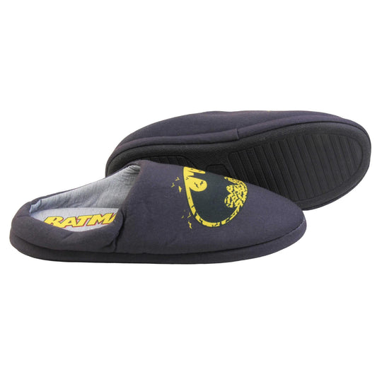 Batman slippers mens. Mule style slippers with black textile upper with a yellow Batman logo on the top. Grey textile lining and firm black sole. Both feet from a side profile with the left foot on its side behind the the right foot to show the sole.