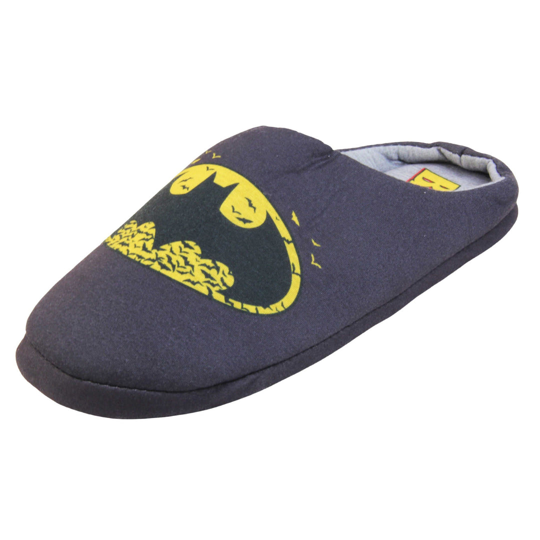 Batman slippers mens. Mule style slippers with black textile upper with a yellow Batman logo on the top. Grey textile lining and firm black sole. Left foot at an angle.