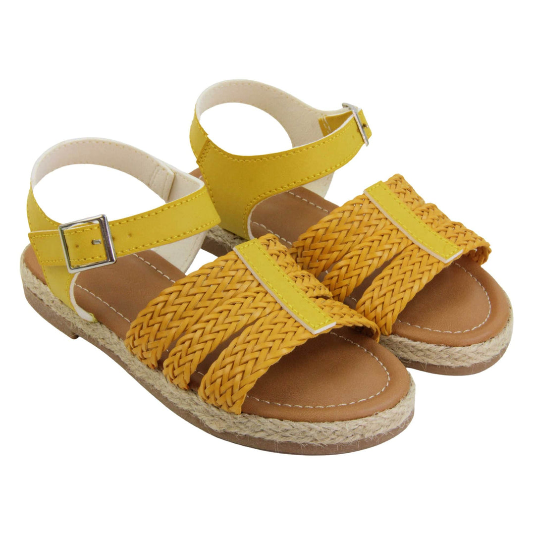 Big kids sandals. Triple strap sandals with a faux leather mustard yellow upper. Three woven faux leather straps over the foot with a plain band down the middle. A plain ankle strap with silver buckle. Brown insole with white lining. Brown outsole with jute rope style rim around the outside. Both feet together at an angle.
