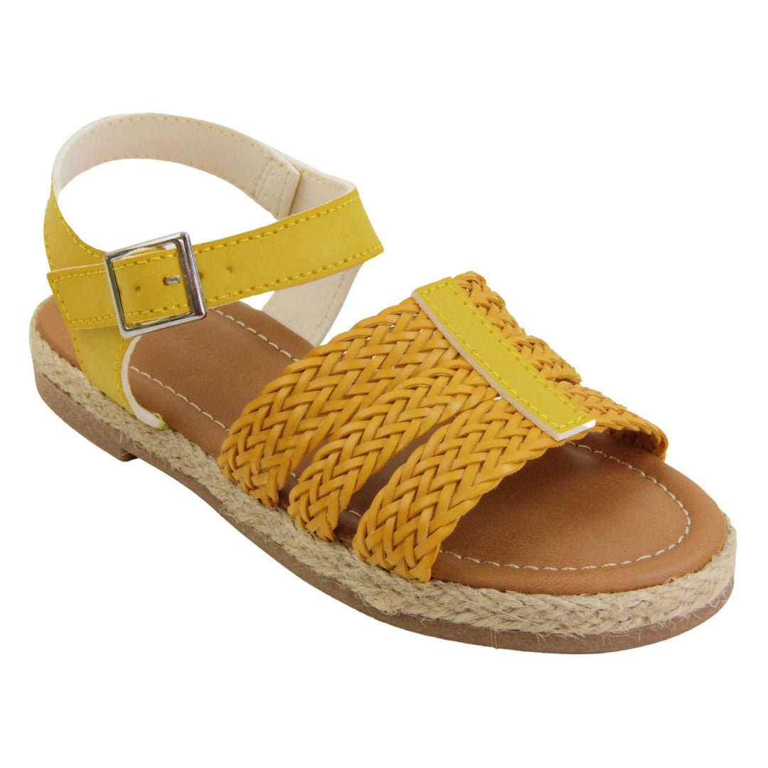 Big kids sandals. Triple strap sandals with a faux leather mustard yellow upper. Three woven faux leather straps over the foot with a plain band down the middle. A plain ankle strap with silver buckle. Brown insole with white lining. Brown outsole with jute rope style rim around the outside. Right foot at an angle.