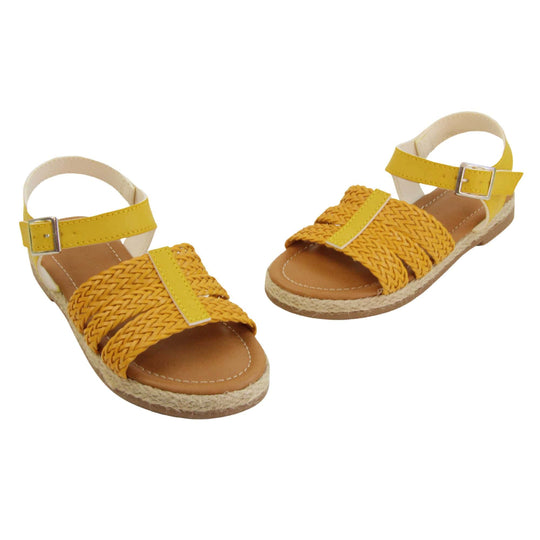 Big kids sandals. Triple strap sandals with a faux leather mustard yellow upper. Three woven faux leather straps over the foot with a plain band down the middle. A plain ankle strap with silver buckle. Brown insole with white lining. Brown outsole with jute rope style rim around the outside. Both feet in a wide V shape with the toes almost touching.