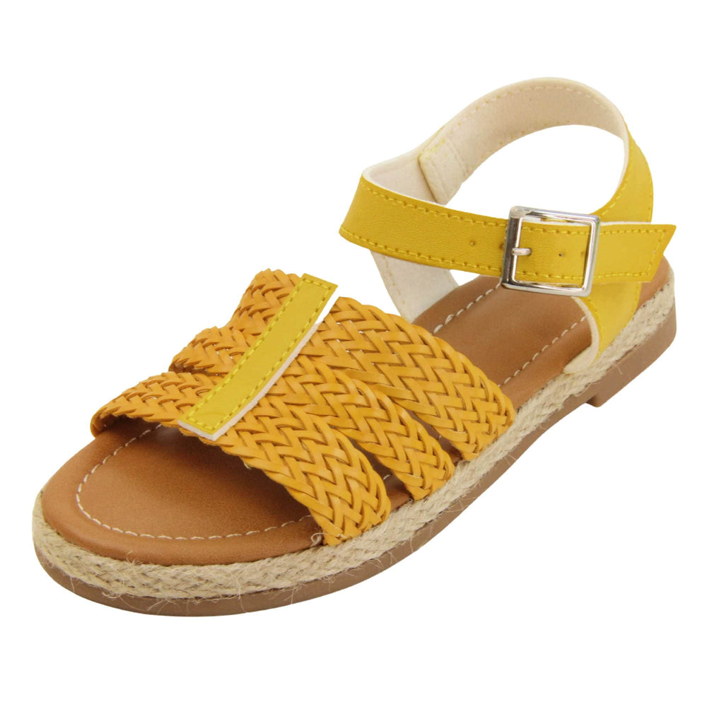 Big kids sandals. Triple strap sandals with a faux leather mustard yellow upper. Three woven faux leather straps over the foot with a plain band down the middle. A plain ankle strap with silver buckle. Brown insole with white lining. Brown outsole with jute rope style rim around the outside. Left foot at an angle.