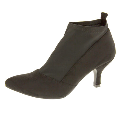 Black faux suede ankle boots. Womens black faux suede ankle boot with a stretchy black fabric panel to the front and around the top of the ankle. Small faux suede loop to the back for pulling onto your feet. Small black faux suede heel and black sole. Left foot at an angle.
