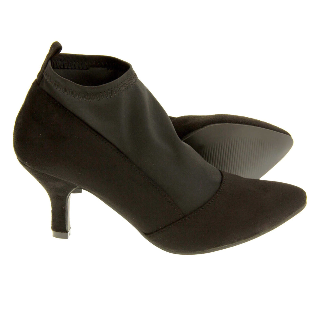 Black faux suede ankle boots. Womens black faux suede ankle boot with a stretchy black fabric panel to the front and around the top of the ankle. Small faux suede loop to the back for pulling onto your feet. Small black faux suede heel and black sole. Both feet from a side profile with the left foot on its side behind the the right foot to show the sole.