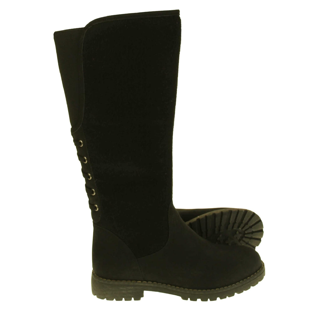 Black knee high boots with zip. Tall boots with a black faux nubuck leather and felt upper with an elastic panel and decorative laces to the back. Stitching detailing around the outsole and the ankle. Full length zip to the inside leg. Both feet from a side profile with the left foot on its side to show the sole.