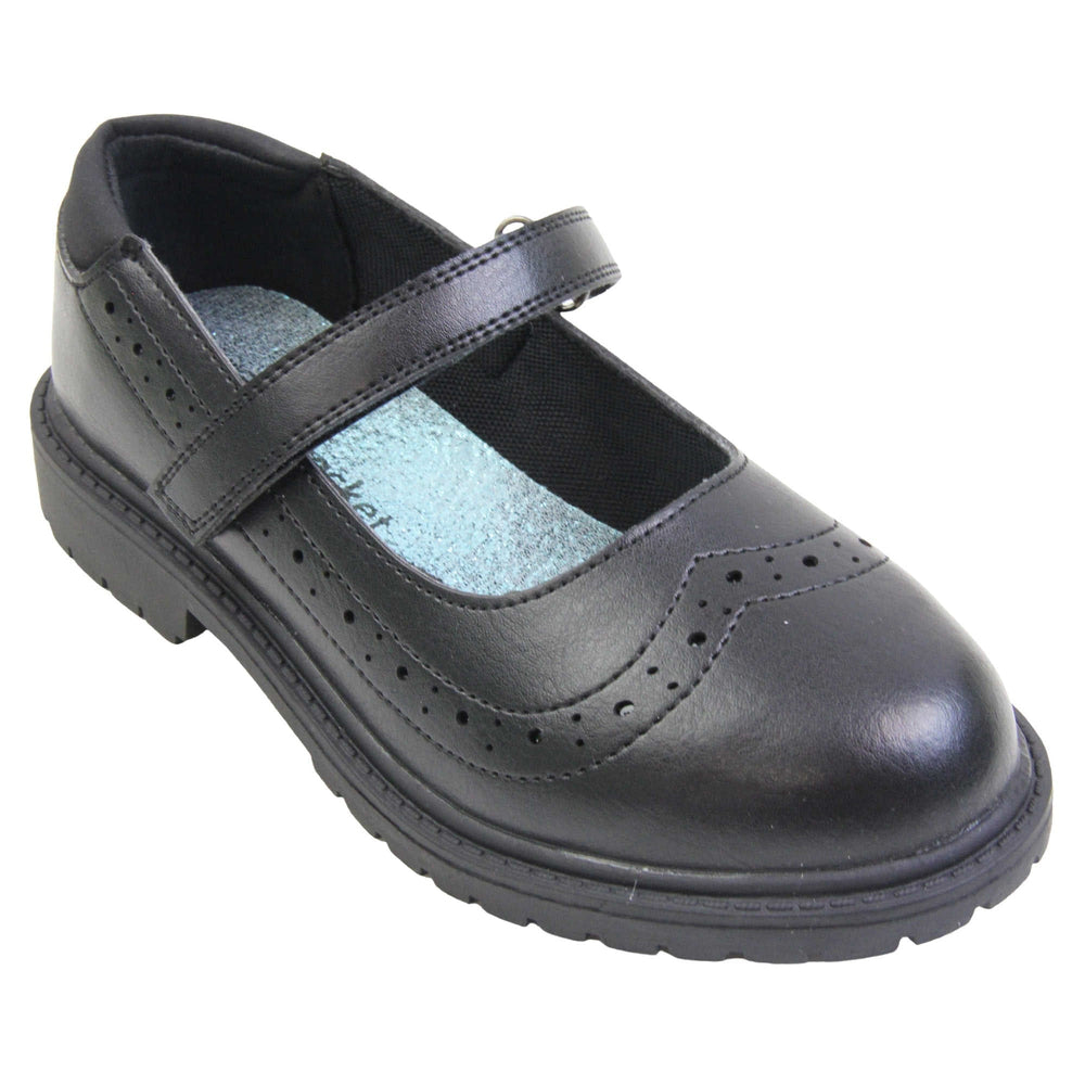 Black school shoes for teenage girls. Mary Jane style shoes with black faux leather uppers. With a touch fasten strap over the foot and brogue detailing around the top of the shoe. Black textile lining with a metallic blue insole. Chunky black sole with slight heel. Right foot at an angle.