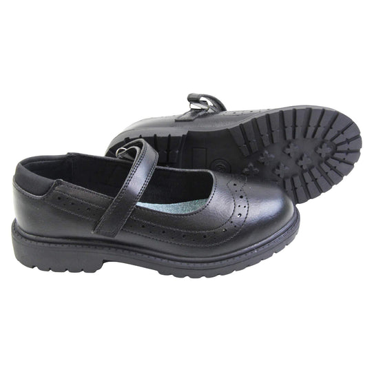 Black school shoes for teenage girls. Mary Jane style shoes with black faux leather uppers. With a touch fasten strap over the foot and brogue detailing around the top of the shoe. Black textile lining with a metallic blue insole. Chunky black sole with slight heel. Both feet from a side profile with the left foot on its side behind the the right foot to show the sole.