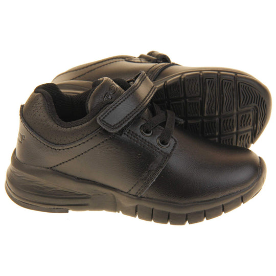 Black School Shoes. Matt black coated leather trainer shoes. With black sole and elasticated lace detailing and touch fastening strap to the top. Both feet from the side but with the left shoes on its side to show the sole.