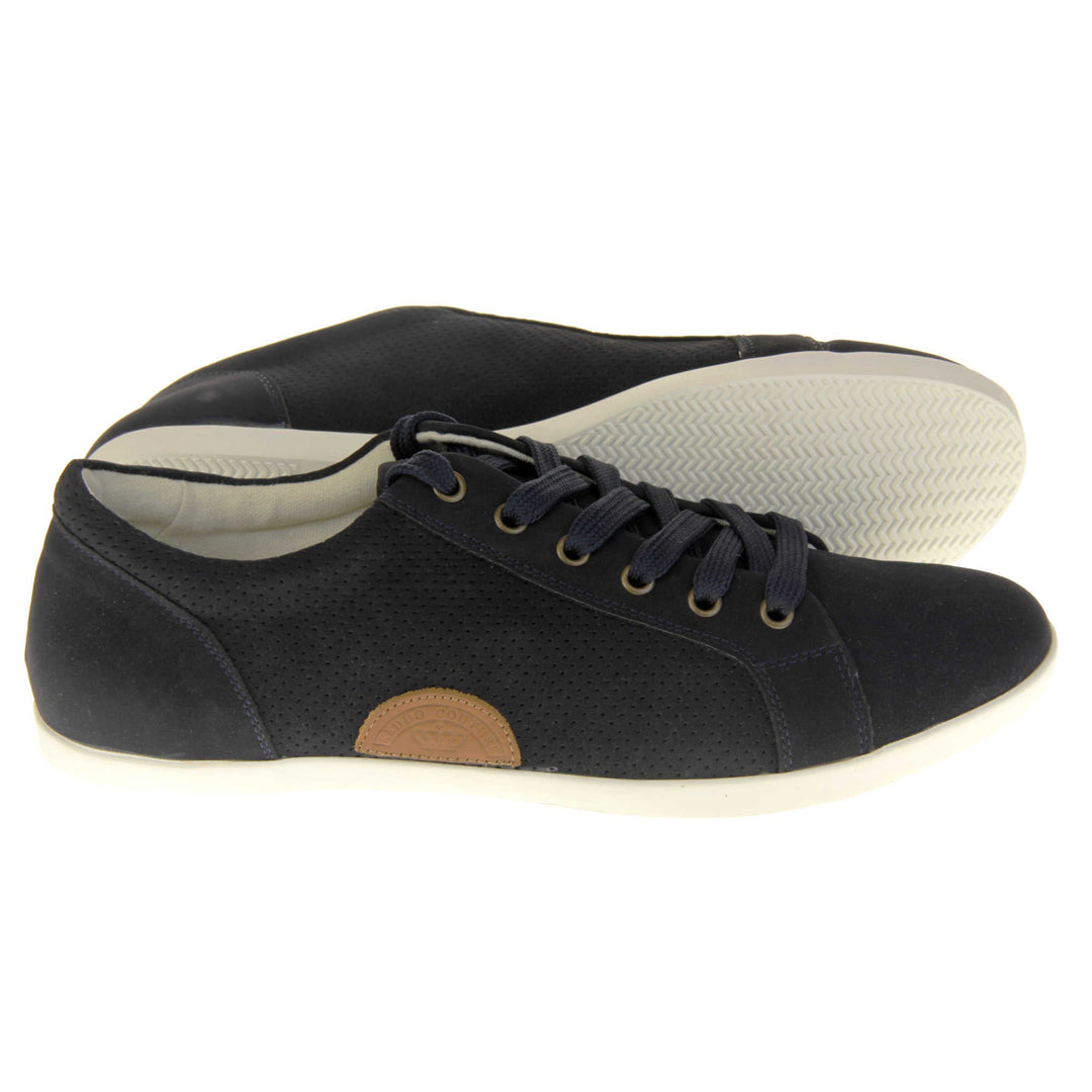 Black suede trainers. Women's shoes in a sneaker style with a black faux suede upper. Tiny dot cut-out detailing to the side of the shoe. Black laces and a brown half-circle to the side of the shoe with Keddo branding on it. White leather lining and sole. Both feet from a side profile with the left foot on its side behind the the right foot to show the sole.