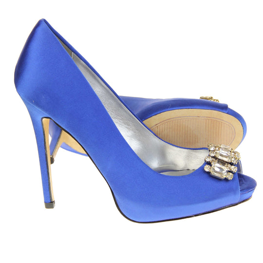 Blue peep toe shoes. Classic women's peep toe high heels with a blue satin upper. Metallic silver insole with Sabatine branding. Blue satin stiletto heel with a cream sole. Diamante cluster detailing across the toes. Both feet from a side profile with the left foot on its side behind the the right foot to show the sole.