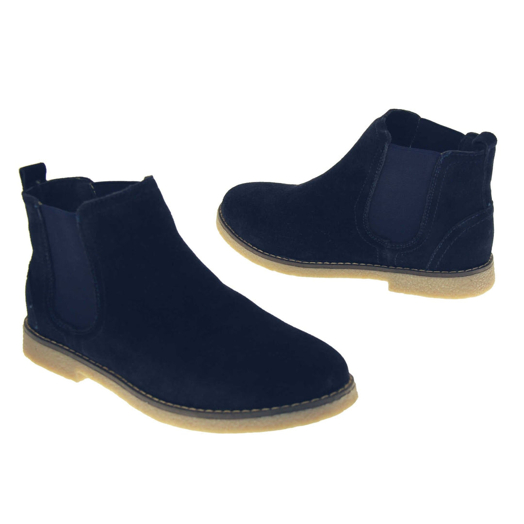 Blue suede ankle boots. Womens Chelsea boot style with a navy blue suede upper. Navy elasticated panels at the ankles and a navy loop at the heel to help pull them on. Beige coloured sole with a very slight heel. Both feet from a slight angle facing top to tail.