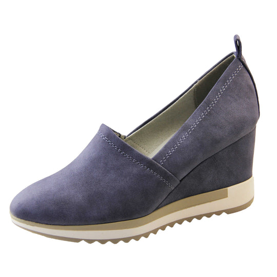 Blue wedge shoes. Womens slip on shoes with a blue faux leather upper. Blue loop to the back to help slip them on. Cream lining. blue faux leather wedge heel with chunky white and beige platform outsole. Beige sole with bumpy tread for grip. Left foot at an angle.