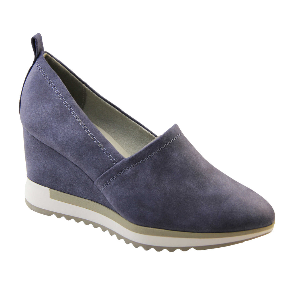 Blue wedge shoes. Womens slip on shoes with a blue faux leather upper. Blue loop to the back to help slip them on. Cream lining. blue faux leather wedge heel with chunky white and beige platform outsole. Beige sole with bumpy tread for grip. Right foot at an angle.