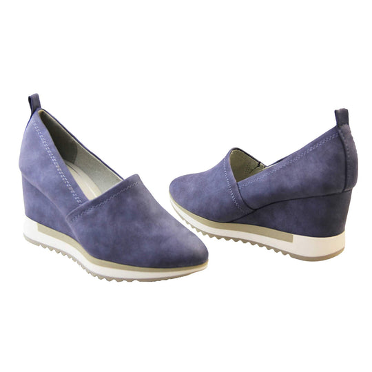 Blue wedge shoes. Womens slip on shoes with a blue faux leather upper. Blue loop to the back to help slip them on. Cream lining. blue faux leather wedge heel with chunky white and beige platform outsole. Beige sole with bumpy tread for grip. Both feet at an angle facing top to tail.