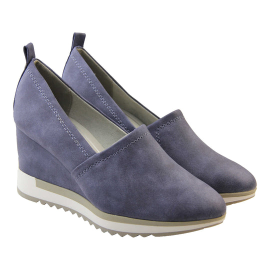 Blue wedge shoes. Womens slip on shoes with a blue faux leather upper. Blue loop to the back to help slip them on. Cream lining. blue faux leather wedge heel with chunky white and beige platform outsole. Beige sole with bumpy tread for grip. Both feet together at a slight angle.