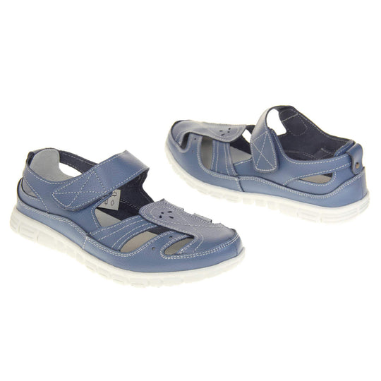 Blue wide fit sandals. Mary Jane style shoes. Blue leather uppers with white stitching detail. Blue touch fasten strap over the foot. Cut outs in the middle, edges and heel of the shoes. White sole with grip to the bottom. Both shoes about an inch apart at a slight angle facing top to tail.