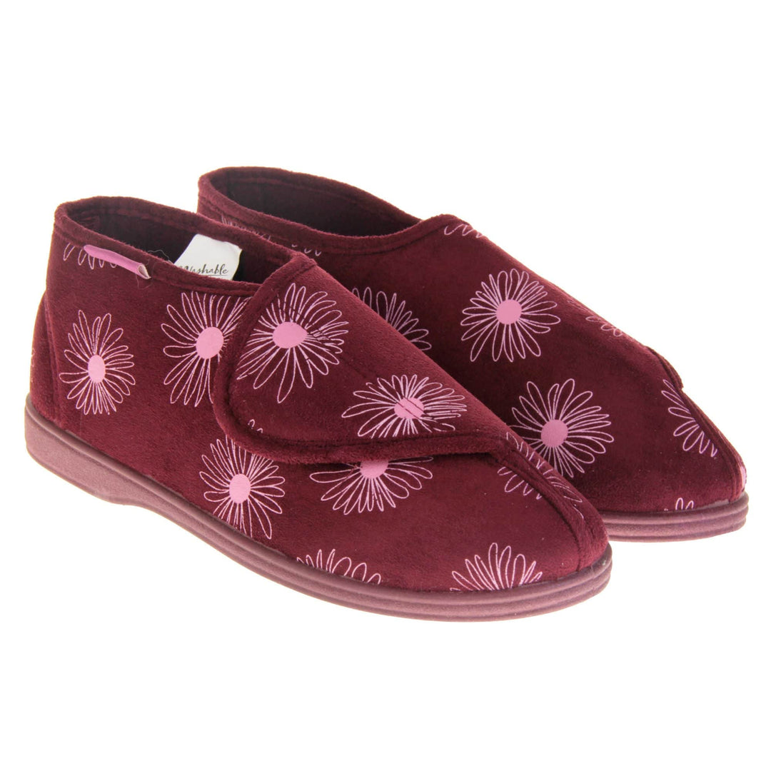 Boot slippers with hard sole. Womens bootie style slipper with a burgundy textile upper with a pink flower print. Touch fasten tab to the top and red textile lining. Firm red sole. Both feet together at angle.