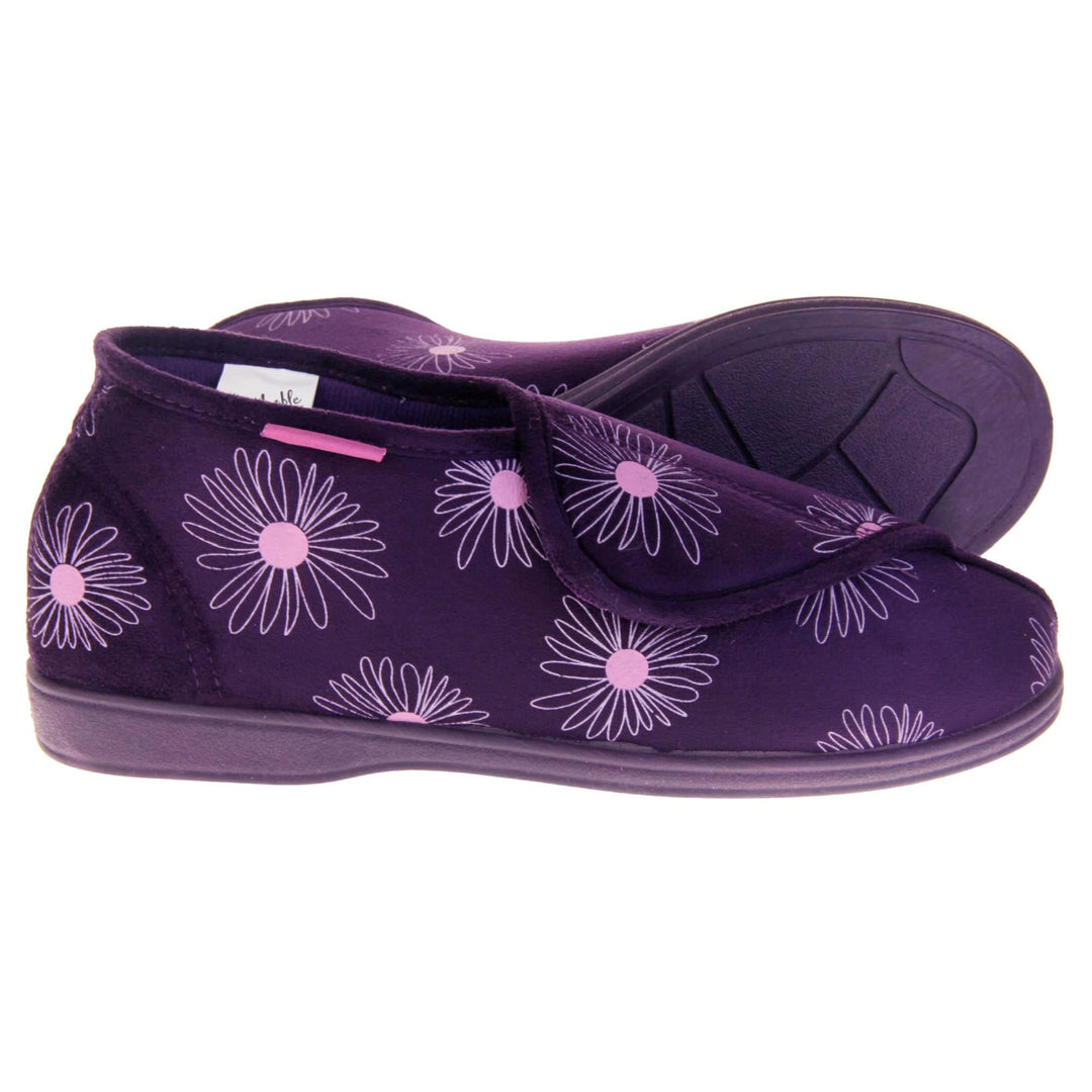 Bootie slippers. Womens bootie style slipper with a purple textile upper with a pink flower print. Touch fasten tab to the top and purple textile lining. Firm purple sole.  Both feet from a side profile with the left foot on its side behind the the right foot to show the sole.