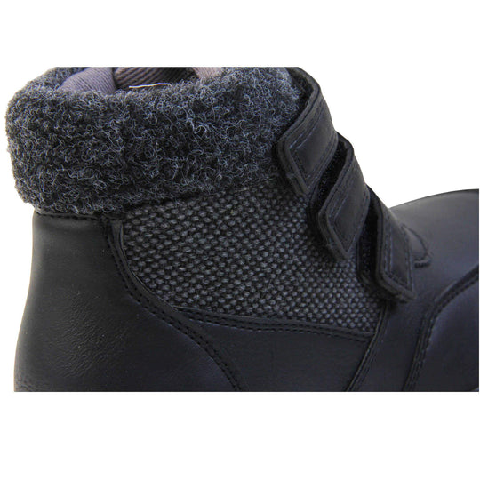 Boys Ankle Boots. Black faux leather upper with textile side panels and black faux fur collar. Three black touch fasten faux leather straps along the front. Grey synthetic sole with grip to the base. Close up of right foot to show the fur collar and textile side panel.