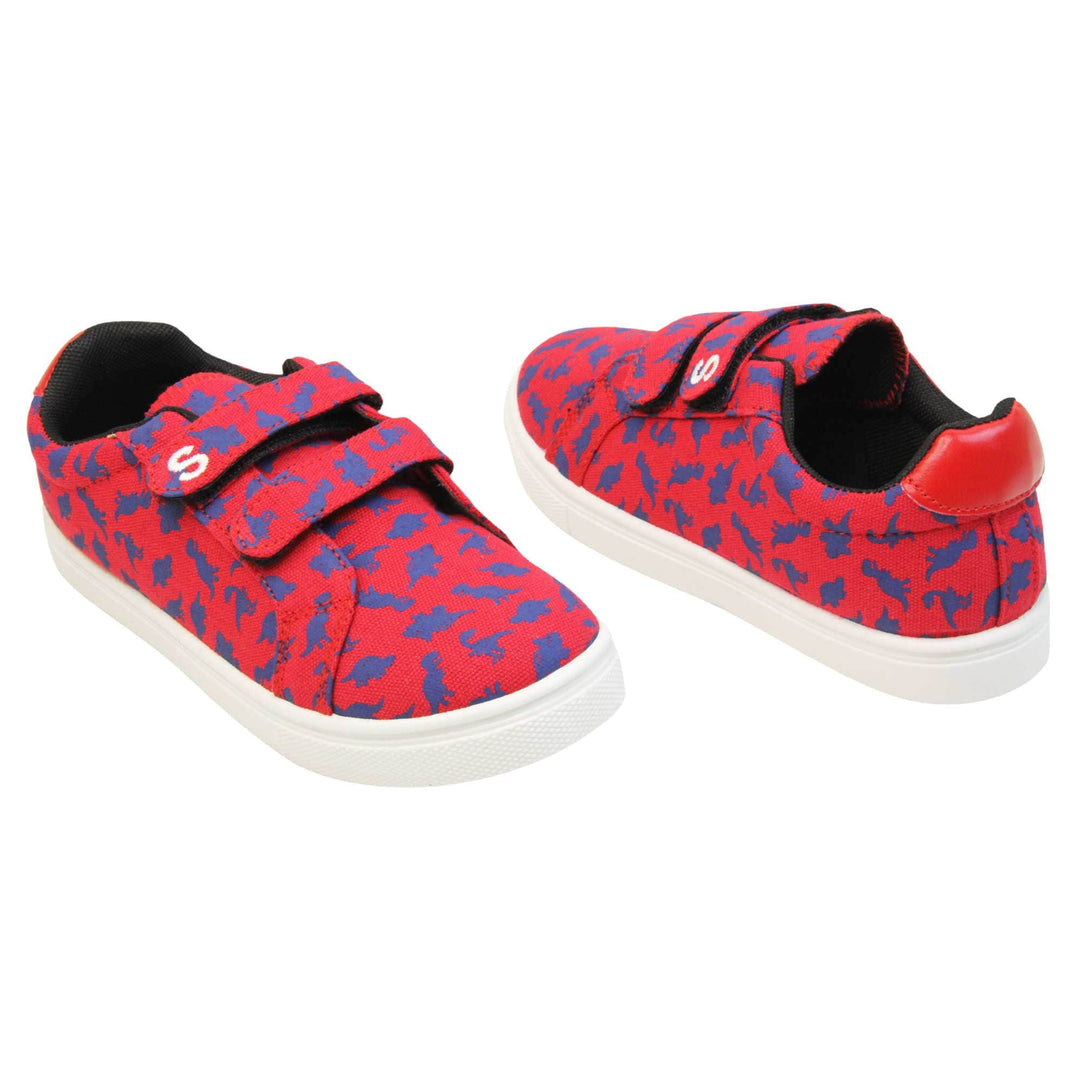 Boys dinosaur shoes. Kids trainers with a red canvas upper with blue dinosaur print. Two touch fasten straps over the top of the shoe with the top strap having the Skyrocket S logo on the end. Black textile lining and white chunky sole. Both feet at an angle facing top to tail.