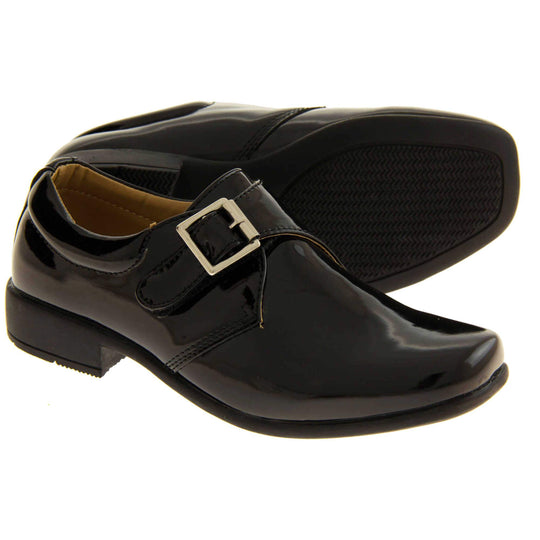 Boys Formal Shoes. Black patent monk style shoes with a buckle effect touch close fastening and a black sole. Both feet with the left foot on its side to show the sole