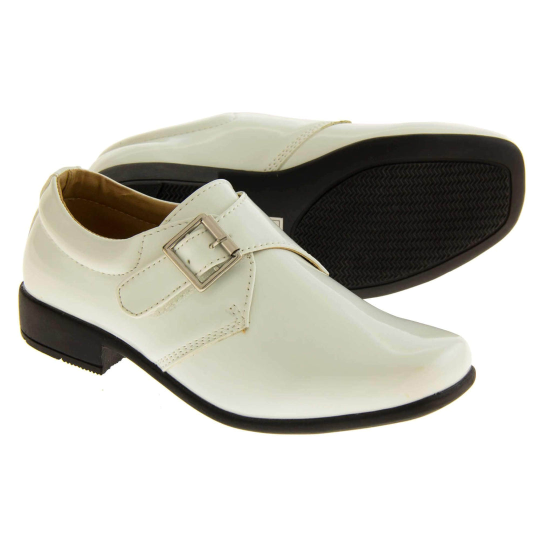 Boys Formal Shoes. White patent monk style shoes with a buckle effect touch close fastening and a black sole. Both feet with the left foot on its side to show the sole