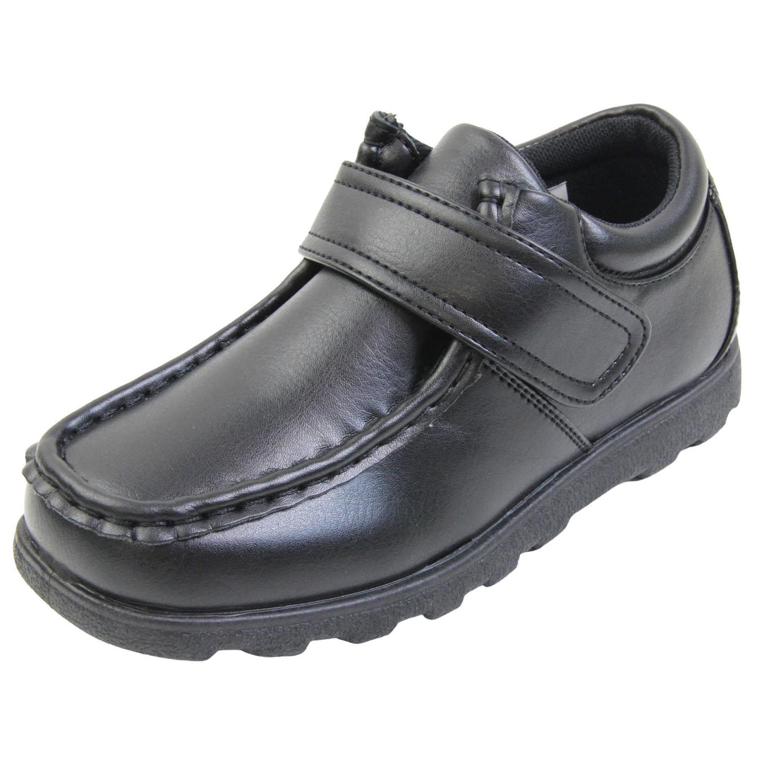Boys smart school shoes. Black low top shoes with faux leather uppers. Stitching detail with a squared toe and a touch fasten strap over the top of the shoe. Black textile lining with light blue insole and black sole with chunky grip. Left foot at an angle.