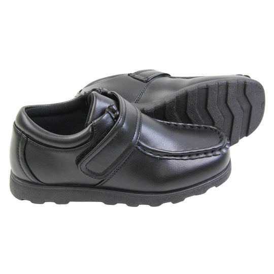 Boys smart school shoes. Black low top shoes with faux leather uppers. Stitching detail with a squared toe and a touch fasten strap over the top of the shoe. Black textile lining with light blue insole and black sole with chunky grip. Both feet from a side profile with the left foot on its side behind the the right foot to show the sole.