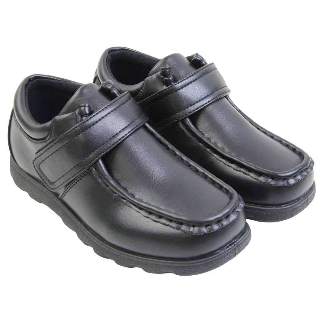 Boys smart school shoes. Black low top shoes with faux leather uppers. Stitching detail with a squared toe and a touch fasten strap over the top of the shoe. Black textile lining with light blue insole and black sole with chunky grip. Both feet together at an angle.