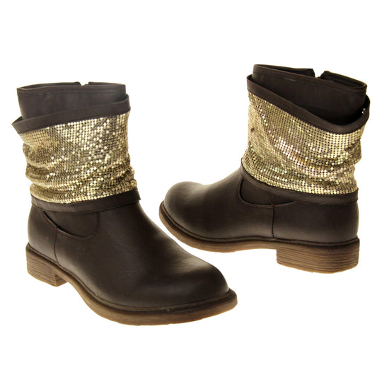 Brown faux leather ankle boots. Biker style boots with a dark brown upper. A thick band of shiny gold chainmail runs around the ankle. Zip fastening down the inside of the boot. Brown sole with a slight heel. Both feet from a slight angle facing top to tail.