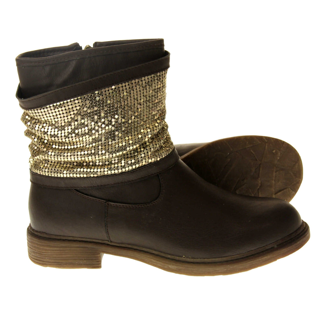 Brown faux leather ankle boots. Biker style boots with a dark brown upper. A thick band of shiny gold chainmail runs around the ankle. Zip fastening down the inside of the boot. Brown sole with a slight heel. Both feet from a side profile with the left foot on its side to show the sole.