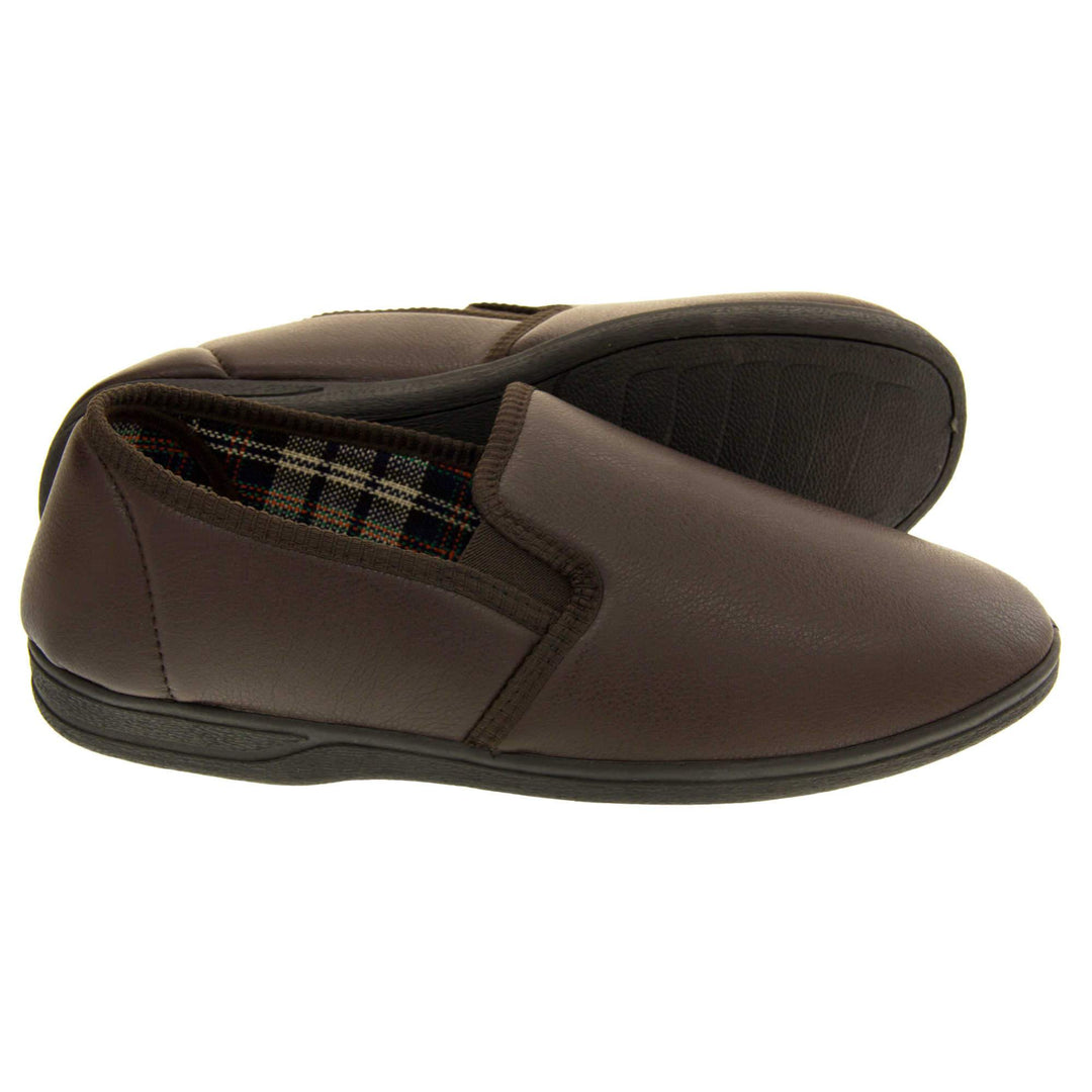 Brown faux leather slippers. Brown faux leather upper with a classic full back slipper design. Twin brown elasticated gussets to the collar of the shoe. Tartan textile lining. Black outdoor sole. Both feet from side profile with left foot on its side to show the sole.