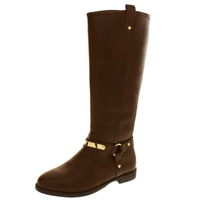 Brown leather boots women. Knee high style boots with a dark brown faux leather upper. A Tri strap going around the ankle and down to the bottom of the boot joined by the ankle with a good loop. Gold plate to the front of the ankle strap. Zip up the inside of the boot. Faux leather loop on the top of the outside of the boot to help with pulling it on. Left foot at an angle.