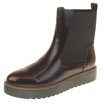 Burgundy flat ankle boots. Faux leather, tall Chelsea boot style with a dark red Bordeaux coloured upper. Black elasticated panels at the ankles and a red loop at the heel to help pull them on. Black coloured low platform sole. Left foot at an angle