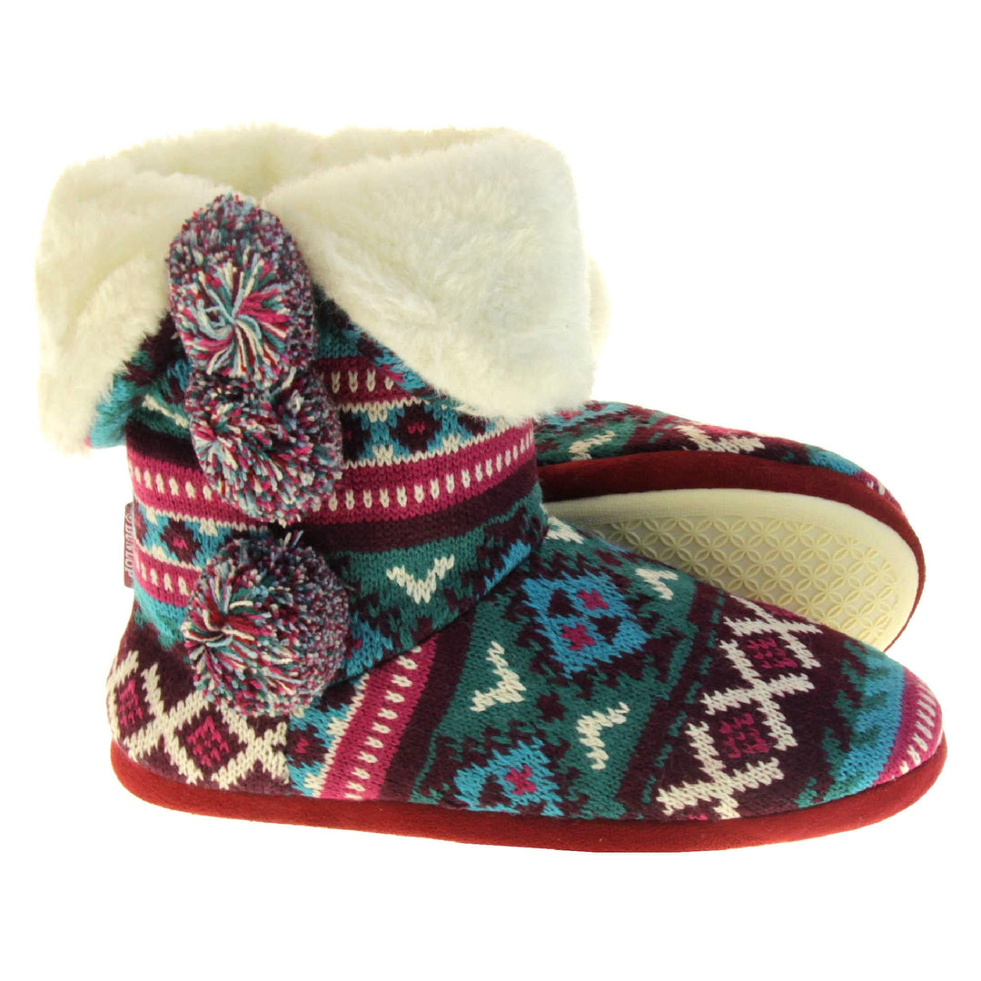 Cable knit slipper boots. Multi coloured patterned knit upper in Aztec style with pom poms to the side, light beige plush faux fur trim and lining. Both feet from a side profile with the left foot on its side behind the the right foot to show the sole.